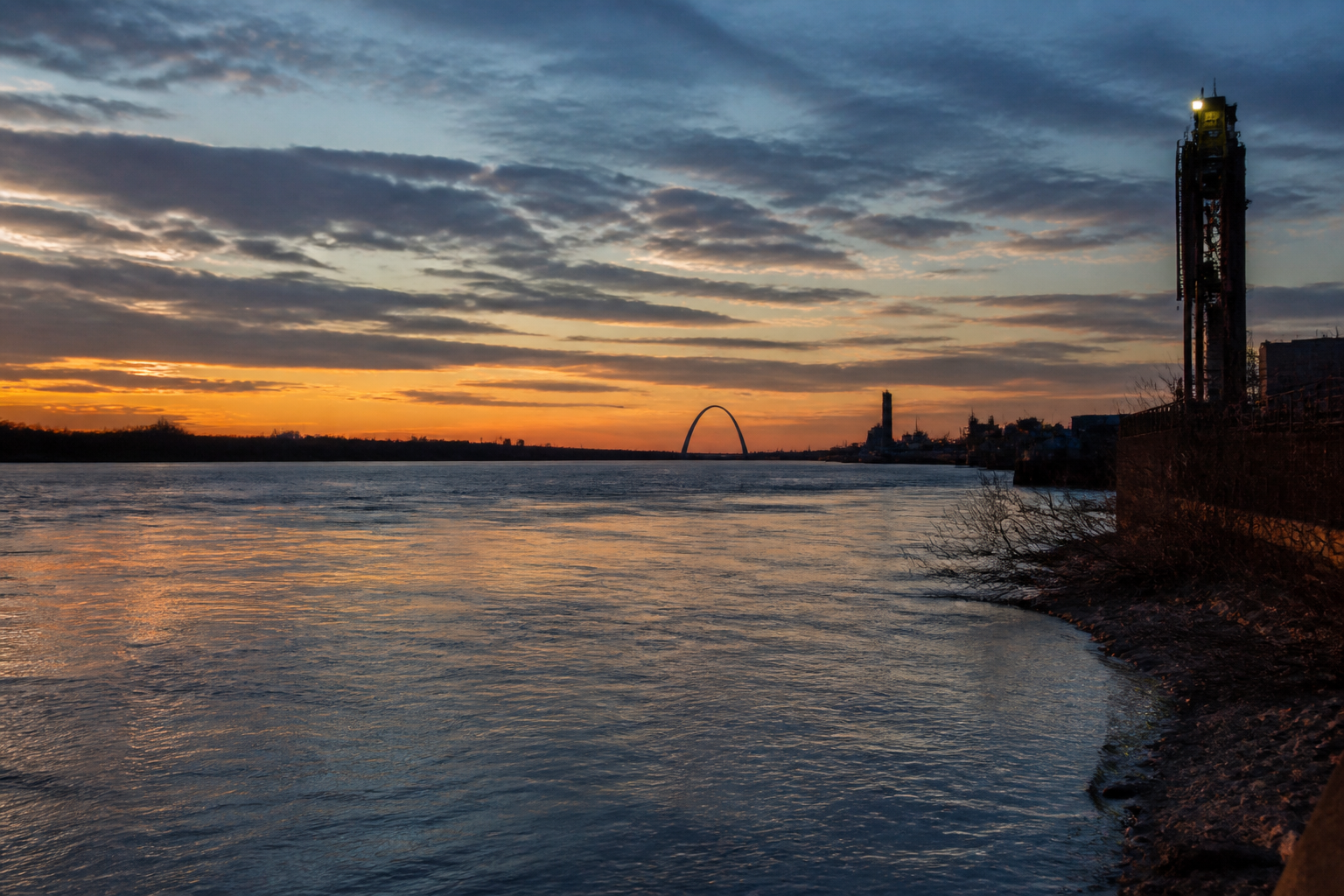The Mississippi River at dusk with a distant pale arch on the horizon.
